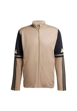 Beige Sportjacke mit Reißverschluss, schwarzen Ärmeln und drei schwarzen Streifen an jedem Arm. Glatte Textur mit hohem Kragen. Mit Adidas-Logo.