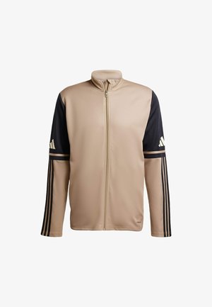 Beige zip-up sportsjakke med sorte ærmer og tre sorte striber på hver arm. Glat tekstur med høj krave. Viser Adidas-logo.