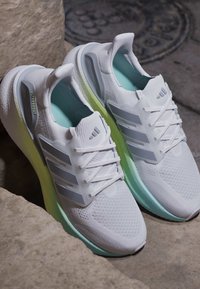 Paire de chaussures de course Adidas Ultraboost blanches avec semelles vert clair reposant sur des marches en pierre.
