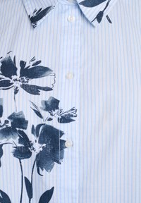 Camisa de rayas azul claro con grandes patrones florales oscuros, cuello clásico y botones blancos. El material parece suave y ligero.
