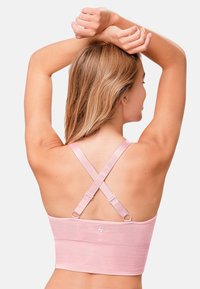 Ljusrosa sport-BH i ett strukturerat material. Har korsade axelband och justerbar hårdvara. Slät yta utan ytterligare mönster.