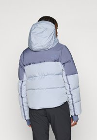 Kerge puffer-jakk helesinisena tumedate hallide aktsentidega. Omab kapuutsi, tikandi disaini ja elastseid mansette tiheda sobivuse jaoks.