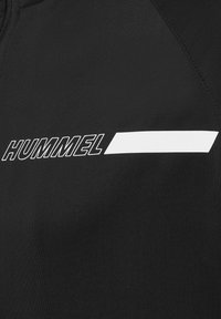 Svart sportkläder med ordet "HUMMEL" i vit text och en horisontell vit detalj, som framhäver en slät textur och sportig design.