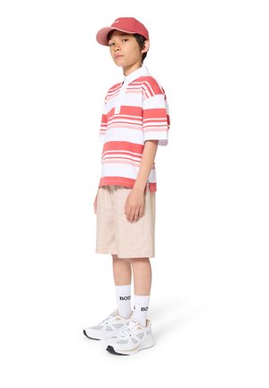 Red and white striped polo shirt, beige shorts, white sneakers with gold accents, and a pink cap. Casual outfit for summer wear.