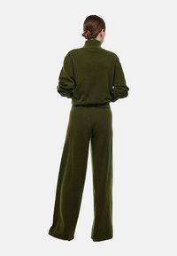 Ensemble en tricot vert foncé composé d'un pull et d'un pantalon large. Le pull présente un col montant et des manches amples, tandis que le pantalon a une coupe décontractée et une texture lisse.