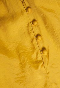 Żółty materiał o gładkiej fakturze, z rzędem okrągłych guzików pokrytych tkaniną po boku, tworzący czysty i prosty design.