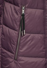 Lila puffjacka med kviltat tyg, sidodragkedja med silverdetaljer och kontrasterande svart dragkedjehandtag.