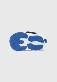 Semelle de sneaker en caoutchouc bleu avec des grips texturés et des accents blancs, présentant une forme arrondie et une languette au talon pour un enfilage facile.