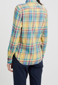 Camicia a maniche lunghe a quadri in tonalità gialle, verdi, rosse e blu. Realizzata in tessuto morbido con orlo curvo e polsini con bottoni.