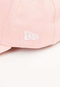 Casquette rose clair en tissu texturé, avec un logo brodé blanc sur le côté. Visière courbée et sangle réglable à l'arrière.