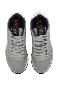 Scarpe sportive grigie realizzate con una combinazione di materiali lisci e testurizzati, dotate di una chiusura con lacci e etichette interne rosse e nere in contrasto.