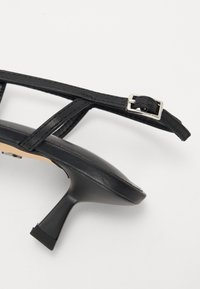 Černé sandály na podpatku s tenkými pásky, vybavené čtvercovou sponou a elegantním, špičatým designem špičky. Hladký kožený povrch.