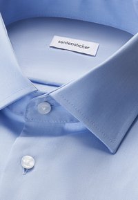 Camicia celeste con colletto classico e due bottoni bianchi chiusi, con etichetta del marchio "seidensticker" all'interno del colletto.