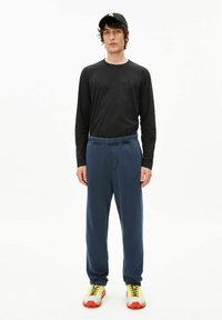 Zwart shirt met lange mouwen, blauwe joggingbroek met elastische tailleband, gele sneakers met rode accenten. Eenvoudige en functionele sportoutfit.