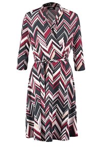 Klänning med omlottstil i svart, vinröd och krämfärgad med ett chevronmönster. Har V-ringning, trekvartsärmar och ett matchande bälte. Slätt tyg.