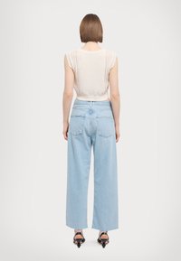 Jasnobeżowy dzianinowy top bez rękawów z teksturowanym wzorem na ramionach, zestawiony z jasnoniebieskimi, szerokimi spodniami z wysokim stanem oraz czarnymi butami na obcasie.