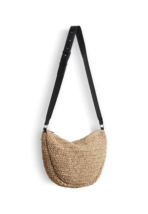 Gevlochten beige schoudertas met een brede verstelbare zwarte band hangend tegen een witte achtergrond.