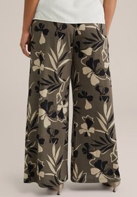 Videbyxor i textil med en blomstrande design i svart och kräm mot en dämpad olivgrön bakgrund.