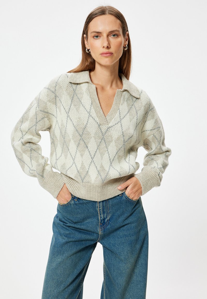 V-Ausschnitt-Rautenmusterpullover in Creme und Hellgrau, mit einem Kragen-Design und gerippten Bündchen, kombiniert mit lockeren blauen Jeans.