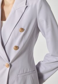 Blazer doppiopetto in lavanda chiaro con bottoni dorati, rever a punta e tasche laterali; tessuto liscio e su misura con vestibilità strutturata.