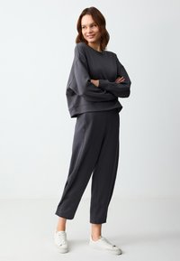 Dunkelgrauer Sweatshirt und passende, schmal zulaufende Jogginghose aus weichem Stoff mit lockerem Sitz. Weiße Sneaker runden den Look ab.