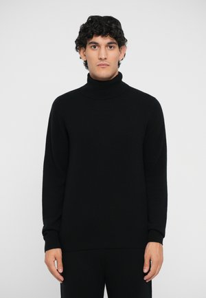 Black knit turtleneck sweater with a smooth texture, relaxed fit, and ribbed cuffs. Model wearing it against a plain white background.