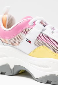 Barevné tenisky s bílou síťovinou a koženými materiály, s růžovými, žlutými a šedými akcenty a texturovanou podrážkou.