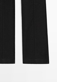 Pantalon noir en tissu tissé, présentant une coupe droite et des coutures visibles. Pas de poches ni d'ornements.