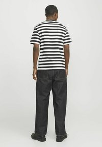 Sort-hvid stribet t-shirt med korte ærmer, parret med mørke denimbukser og sorte sko, set fra ryggen.