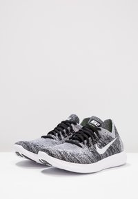 Scarpe da corsa Nike in materiale a maglia grigio e nero con suola bianca e logo swoosh, dotate di lacci neri e collo imbottito.