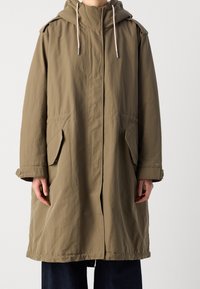 Cappotto impermeabile khaki con cappuccio, chiusura frontale e due tasche laterali. Presenta una vestibilità comoda e un cordino regolabile al collo.
