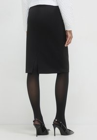 Schwarzer Bleistiftrock mit einem Rückenschlitz, kombiniert mit schwarzen strukturierten Strumpfhosen und High-Heels mit Nietenakzenten. Glatte Stoffoberfläche.