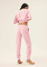 Różowy skrócony sweatshirt z krótkimi rękawami i haftem na plecach, w połączeniu z dopasowanymi dresami z elastycznym pasem. Miękka tkanina i luźny krój.