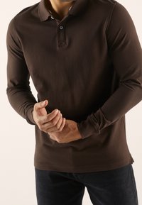 Ruskea pitkähihainen poolopaita, jossa on kaulus, napillinen etulista ja kapea istuvuus. Sileä pinta ja kontrastivärinen sisäkaulus.