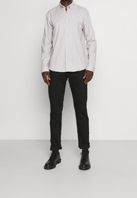 Lichtgrijs long-sleeve overhemd met knopen en kraag, gecombineerd met opgerolde zwarte broek en zwarte leren schoenen. Eenvoudig, klassiek ontwerp.