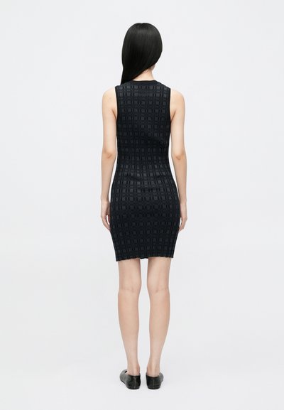 Rochie ajustată fără mâneci, de culoare neagră, cu un model texturat în grilă, până la genunchi, cu o margine dreaptă. Asortată cu pantofi negri, ușor de încălțat.