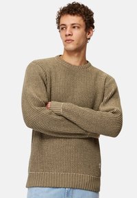 Olivgrön stickad tröja med texturmönster, rundad halsringning och ribbade ärmslut. Sidoflanken har en liten logotagg.