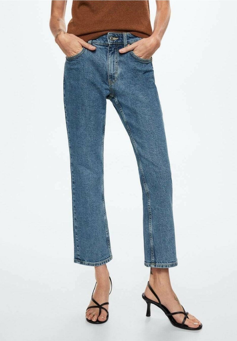 Jean en denim bleu clair à coupe droite, design à cinq poches, ourlets effilochés, associé à des sandales à talons hauts noires avec lanières.