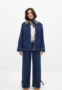 Džinsa jaka ar korduroja apkakli, brīvs griezums. Zili plaši bikses ar saitēm apakšmalā. Slāņos ar svītrainu krekli un šalli.