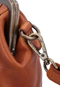 Primer plano de un bolso de cuero marrón que muestra un broche de metal que conecta la correa con el lazo del bolso con textura y costuras visibles.