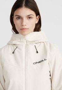 Béžová mikina na zips s kapucňou, s čiernym logom "O'Neill" na hrudi a nastaviteľnými šnúrkami. Hladká, ľahká tkanina.