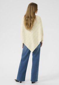 Poncho tricotat din fildeș cu un model în zigzag, având un design triangular și croială liberă. Asortat cu blugi din denim cu picioare largi și bocanci cu toc.