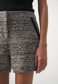 Femme portant un short texturé noir et blanc taille haute avec un détail de poche bordé de noir, associé à un haut noir côtelé sans manches.