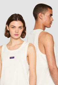 Camisetas sin mangas blancas de algodón, con un escote redondeado y un parche con el logo de GANT en azul y rojo. Diseño simple con costuras mínimas.