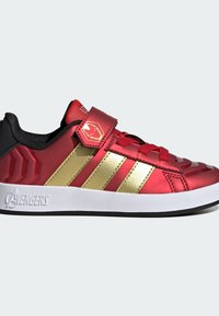 Rød og guld atletiksko med en glat, skinnende overdel, tre guldstriber, teksturerede detaljer, sort inderside og velcrolukning. Hvid sål.