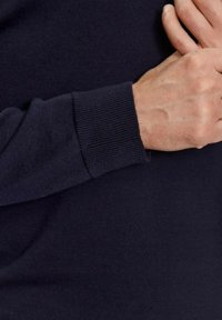 Marineblauwe sweaterstof met geribbelde manchetten, een zachte textuur en een aansluitende snit, met een close-up van de mouw en arm.