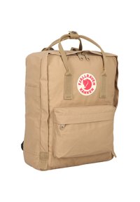 Sandfärgad ryggsäck med rektangulär form, gjord av slitstark tyg. Har en framficka, handtag på toppen och en cirkulär logotyp som accent.