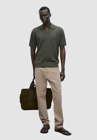 Short-sleeve, ribbed dark green polo shirt, light beige straight-leg trousers, black flip-flops, holding a dark green suede tote bag.