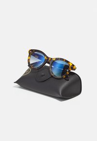 Ochelari de soare tip cat-eye cu ramă de broască țestoasă și lentile gradient albastre, așezați deasupra unei huse din piele neagră texturată, cu închidere tip clapetă.