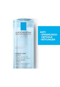 Clear plastic bottle of La Roche-Posay micellar water. Light blue liquid, labeled in black and pink text. Blue square logo at the top.